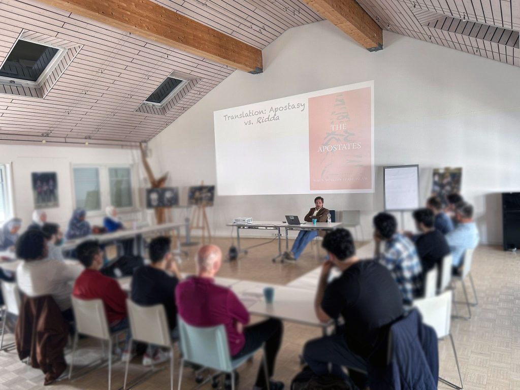 Workshop an Tischen, vorne der Referent vor der Leinwand, Gesichter unscharf